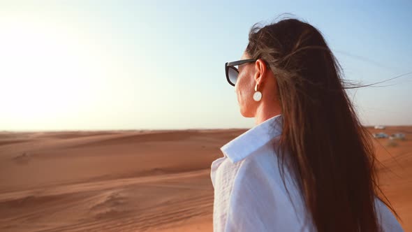 Young Woman Tourist in Dubai Rear View From Back Stands in Desert and Sunbathes Under Sunlight