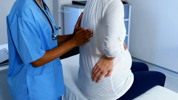 Doctor examining pregnant womans back in ward