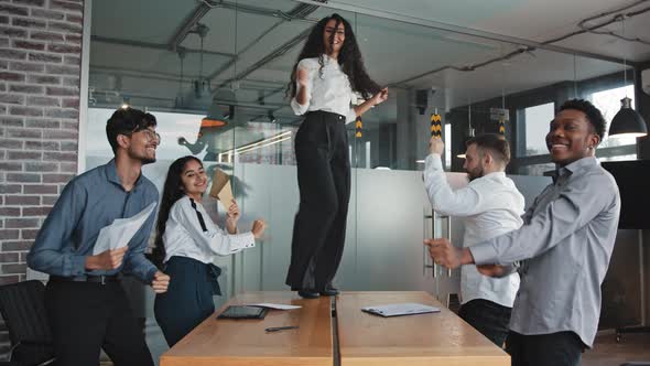Young Incendiary Hispanic Boss Dancing on Table in Boardroom Girl Leader Celebrate Victory with