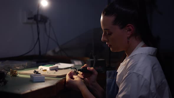 Side View Skilled Female Silversmith Polishing Ring with Manual Tool in Workshop with Blue Light