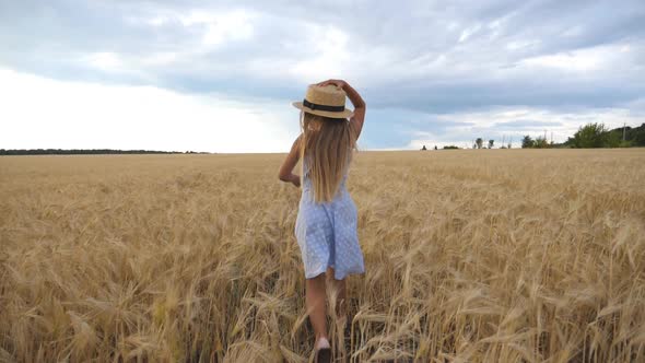 Beautiful Girl with Long Blonde Hair Running Through Wheat Field, Turning To Camera and Smiling