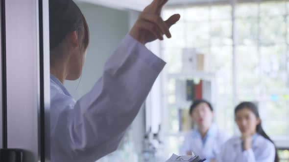 Rear View of Young Female Doctor Holding Clipboard Pointing Towards Glass Door While in a Meeting