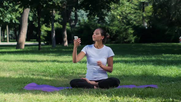 Girl Sitting on a Mat and Doing Selfie with Smart Phone in the Yoga Position