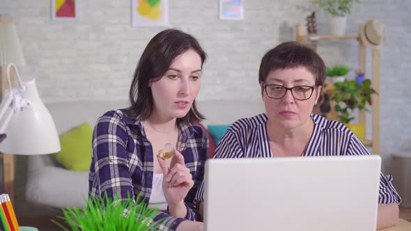 Young Woman Sitting at a Laptop Explains To a Middleaged Woman How To Use a Hearing Aid