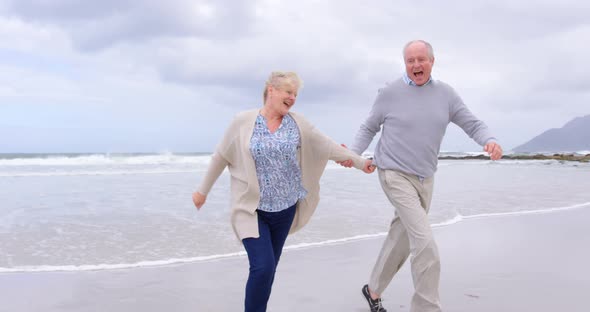 Front view of old caucasian senior couple running on the beach 4k