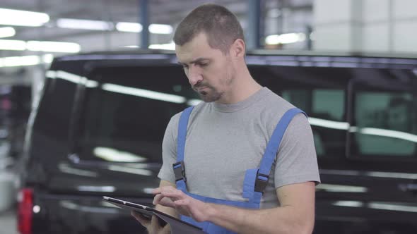 Portrait of Young Handsome Caucasian Man in Workwear Using Tablet, Looking at Camera and Smiling