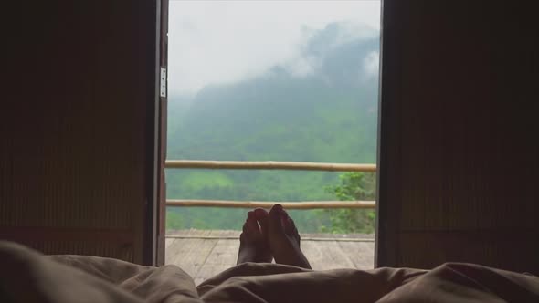 Men's legs stick out from under the blankets and turn to the sidesagainst of the balcony and mountai