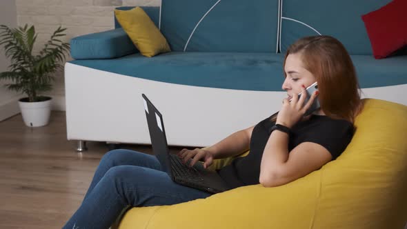 Young Woman Is Working at the Laptop While Is Talking on the Phone.