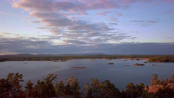 Fly over a Rocky Pine Tree Hill to Reveal Small Granite Islands, Blue Sky and Clouds at Sunset, Dron