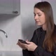 A Young Woman in the Kitchen Uses a Mobile Phone - VideoHive Item for Sale