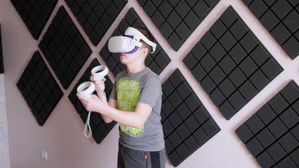 Teenager in 3D Glasses with Game Controllers Plays in a Soundproof Room