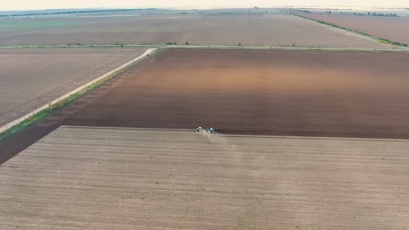 Aerial Shot of a Square Agriculture Area with a Tractor Furrowing It in Autumn