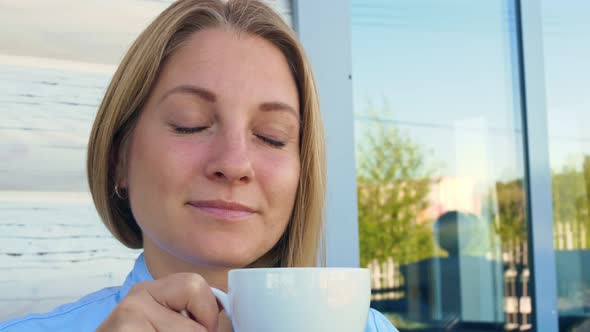 A Beautiful Woman with Blue Eyes Drinks Coffee in the Morning on the Terrace of Her House Looks Into