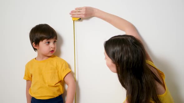 Mom Measures the Growth of a Boy with a Ruler with a Son