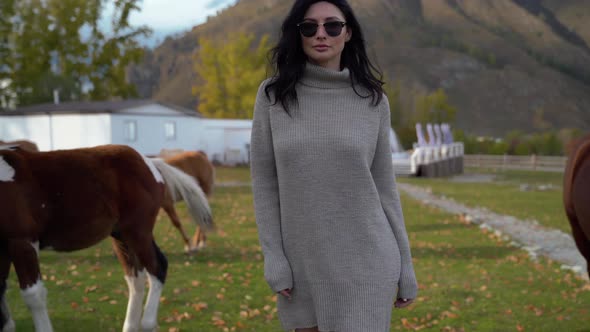 Beautiful Girl with Black Hair in Glasses Walks Around Ranch with Horses