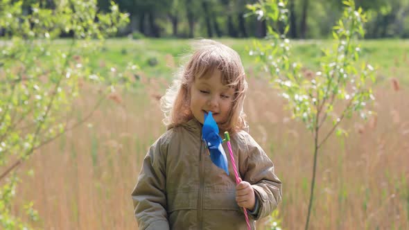 Portrait of Happy Cute Light Hair Little Girl with Windmill Toy. Girl Smiles and Thinks How It Work