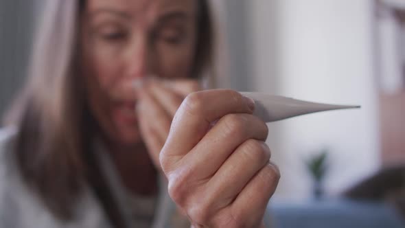 Woman holding a thermometer while blowing her nose at home