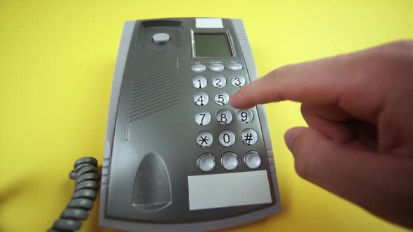 Man Dials Number on Corded Phone Base on Yellow Background