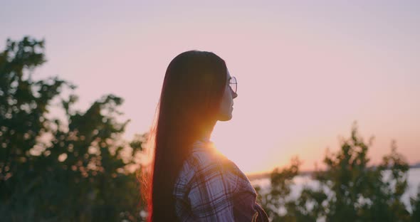 A young girl on the background of sunset looks thoughtfully into the distance