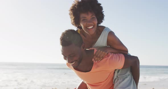 Portrait of smiling african american couple embracing on sunny beach