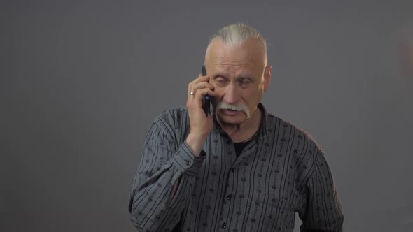 Senior Man with Grey Mustache Talks Holding Black Smartphone