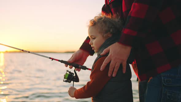Curly Caucasian Little Boy is Learning to Fish Father or Grandpa is Teaching Him Happy Family