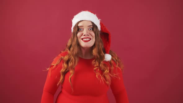 Studio Portrait of Young Amazed Overweight Woman Wearing Santa Hat Looking at Camera Red Background