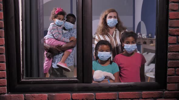 Diverse Family in Face Masks Looking Out Window
