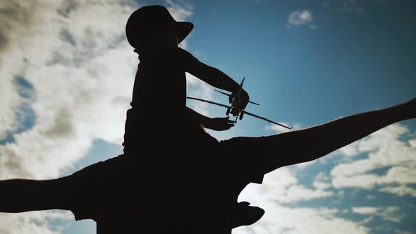 Silhouette Happy Father and Little Son Playing with Airplane Toy Together Against Blue Sky. The Boy