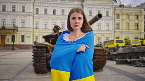 Grieving Ukrainian Woman Covered with Flag Stands Near Tank