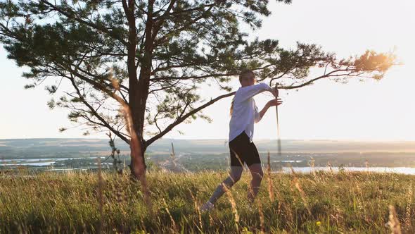 Swords Training Young Pretty Woman in White Shirt Waving with a Sword Outdoors at Early Sunset on