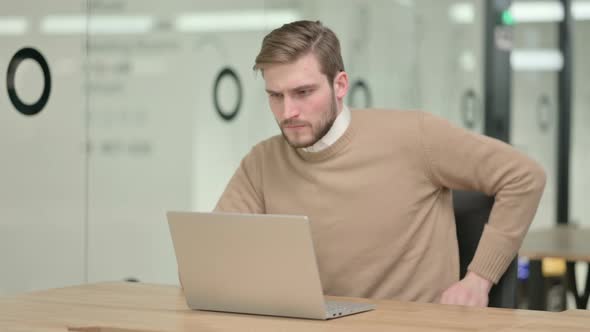 Creative Young Man with Laptop Having Back Pain in Office