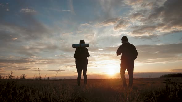 Silhouettes of Two Hikers with Backpacks Enjoying Sunset View From Top of a Mountain
