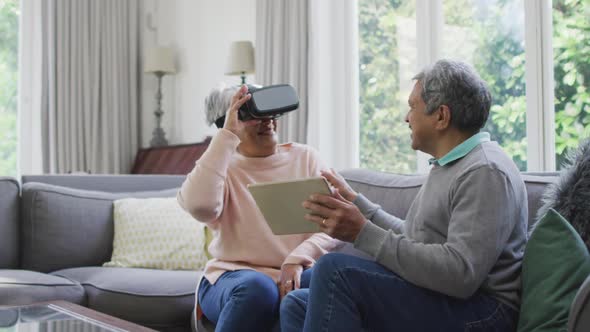 Happy mixed race senior couple wearing vr headset and having fun at home