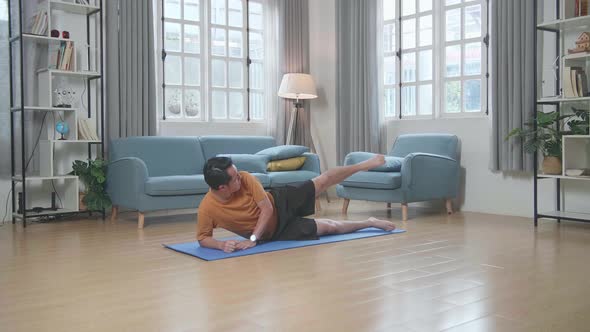 Asian Man Doing Yoga By Side Leg Raise On Mat At Home