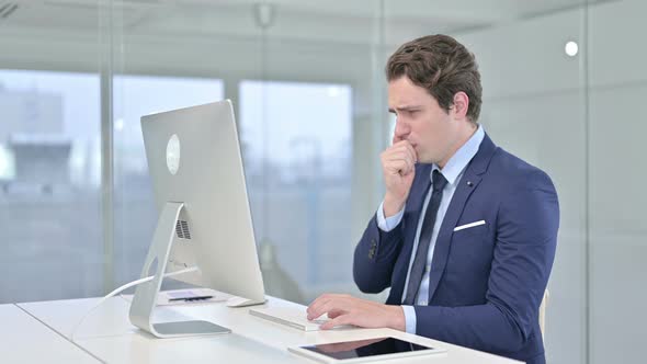 Sick Young Businessman Working on Desk Top and Coughing in Office