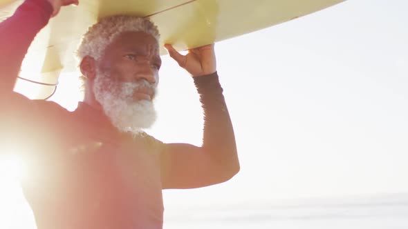 Senior african american man walking with surfboard on sunny beach