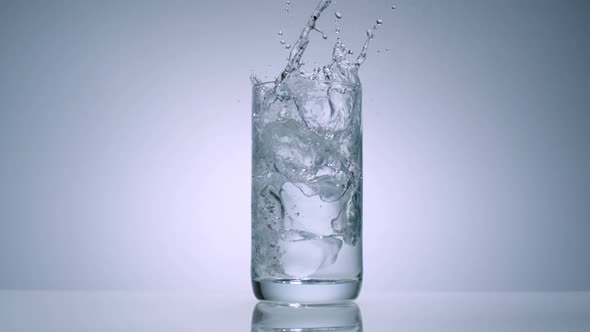 Slo-motion ice cube dropping into glass with water