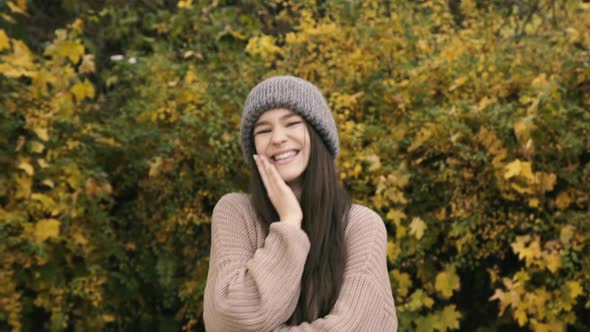 Pretty Girl Poses at Camera Whirls and Undresses Cap in Park