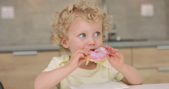 Adorable Little Girl Eats a Donut While Sitting at the Kitchen Table