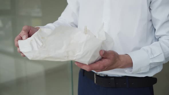 Close View of Male Hands Unwraps Tasty Hamburger To Eat Indoors on Background