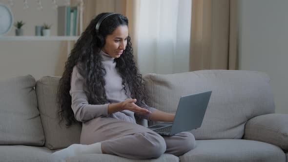 Smiling Young Woman Wave Hand Talking on Video Call Use Laptop and Headphones Positive Hispanic Girl