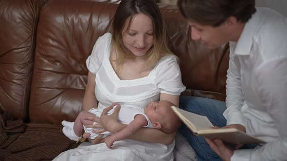 Portrait of Caucasian Woman Shaking Newborn Boy in Slow Motion Sitting on Couch with Man Reading