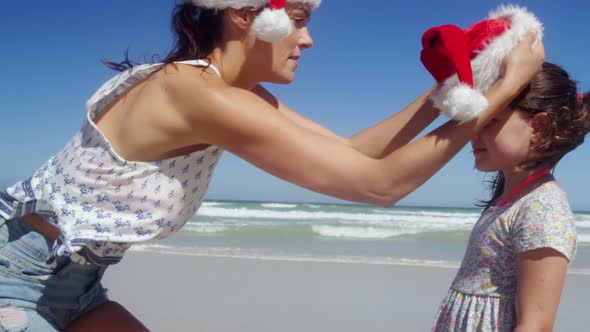 Mother putting santa hat on girl head at beach