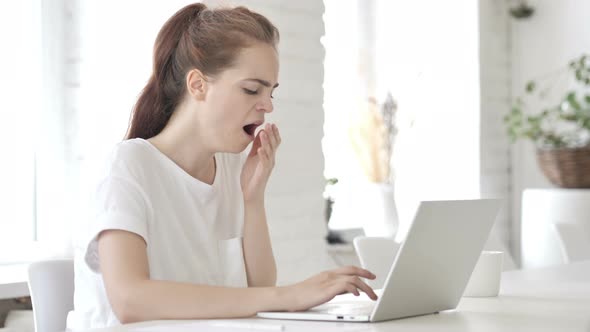 Tired Young Woman Yawning while working on Laptop