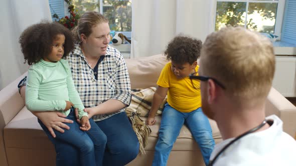 Doctor Visiting Two African Sick Children at Home and Discussing Diagnosis with Caucasian Mother