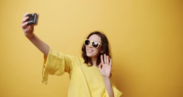 A Young Girl Smiles Takes a Picture with the Retro Camera on a Yellow Background