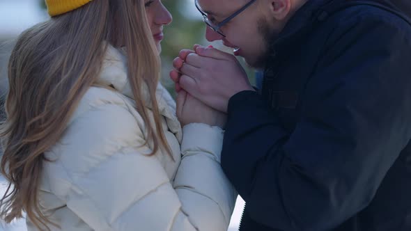 Closeup Boyfriend Warming Girlfriend Hands with Breathe Standing in Sunny Winter Forest Smiling