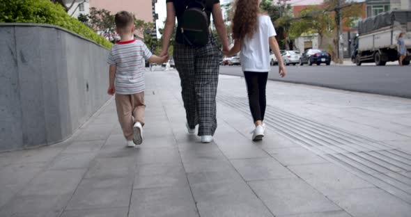 Mom Walks with Two Children Walking Down the Street Holding Hands