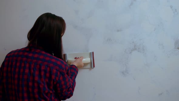 Rear View of Young Woman Polishing Wall with Sandpaper in Room